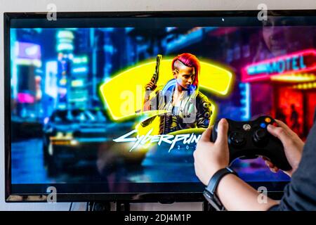 Femme tenant une manette xbox et jouant à un jeu vidéo populaire Cyber-punk 2077 sur un téléviseur et un PC Banque D'Images