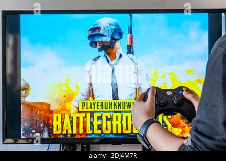 Femme tenant une manette xbox et jouant à un jeu vidéo populaire Player Unknown champ de bataille PUBG sur un téléviseur et un PC Banque D'Images