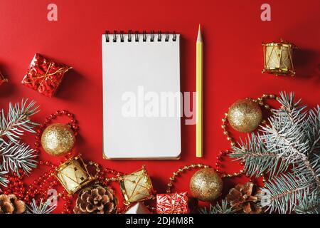 Bloc-notes et crayon pour écrire des voeux et des cadeaux pour le nouvel an et Noël autour des décorations d'arbre de Noël sur un fond rouge. Nouvel an moo Banque D'Images