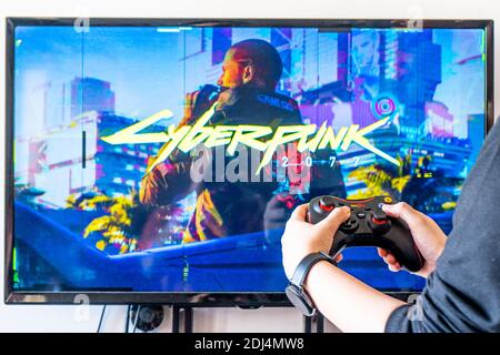 Femme tenant une manette de Red Gear et jouant de la vidéo populaire Jeu Cyberpunk 2077 sur un téléviseur et un PC Banque D'Images