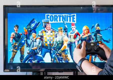 Femme tenant une manette xbox et jouant à un jeu vidéo populaire Fortnite sur un téléviseur et un PC Banque D'Images