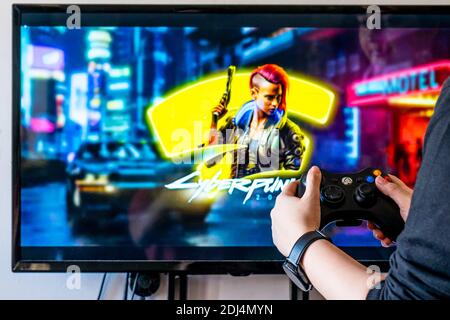 Femme tenant une manette xbox et jouant à un jeu vidéo populaire Cyber-punk 2077 sur un téléviseur et un PC Banque D'Images