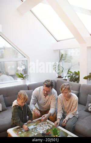 Portrait grand angle vertical de père aimant passer du temps avec deux fils jouent ensemble des jeux de société et des puzzles dans le moderne intérieur de la maison Banque D'Images