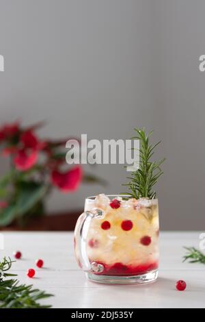 Thé noir froid rafraîchissant avec glace et canneberges, verre avec baies et thé décoré d'une branche de romarin sur fond de bois blanc Banque D'Images