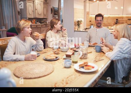 Portrait grand angle de la grande famille heureuse appréciant le petit déjeuner ensemble assis à table dans la cuisine, se concentrer sur le père souriant et trois enfants, l'espace de copie Banque D'Images