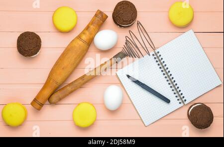 Le processus de fabrication de biscuits au chocolat, macarons, ingrédients sur fond de bois rose. Œufs, rollpin, corolle, cahier de recettes avec stylo. T Banque D'Images