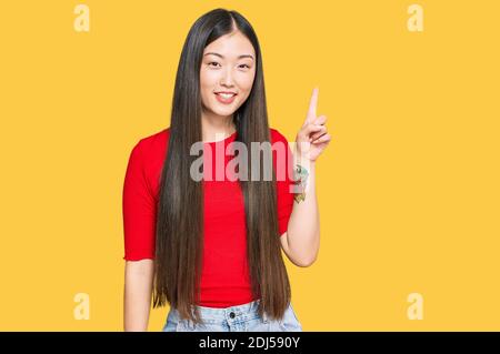 Jeune femme chinoise portant des vêtements décontractés montrant et pointant vers le haut avec le doigt numéro un tout en souriant confiant et heureux. Banque D'Images