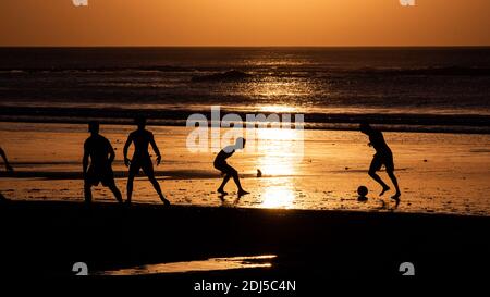 Jeunes jouant au football sur une plage de Bali à coucher de soleil Banque D'Images