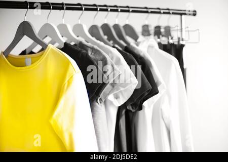 Porte-vêtements avec différentes chemises féminines placés dans une pièce de style minimaliste avec des murs blancs Banque D'Images