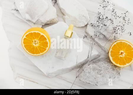 Flacon en verre avec sérum pour le visage disposé sur une table avec des pierres et des oranges mûres Banque D'Images