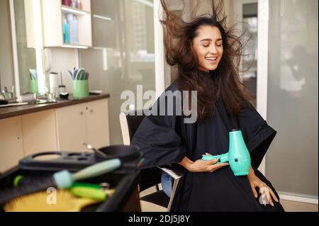 Une cliente heureuse utilisant un sèche-cheveux, un salon de coiffure Banque D'Images