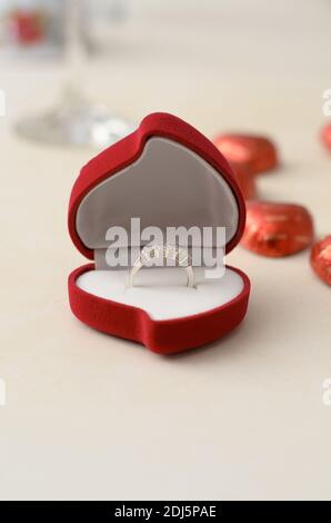 Bague d'argent dans une boîte rouge en forme de coeur, sur une table blanche sur fond de bonbons Banque D'Images