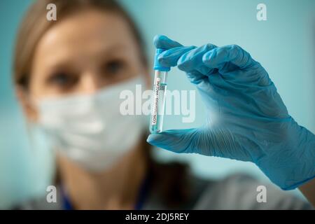 Main gantée de jeune chercheuse contemporaine ou de laboratoire médical travailleur tenant une petite fiole avec un échantillon de nouveau vaccin Banque D'Images