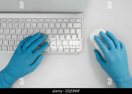 Aperçu des mains gantées d'un professionnel de la santé contemporain en cliquant sur un ordinateur souris et boutons du clavier par poste de travail Banque D'Images