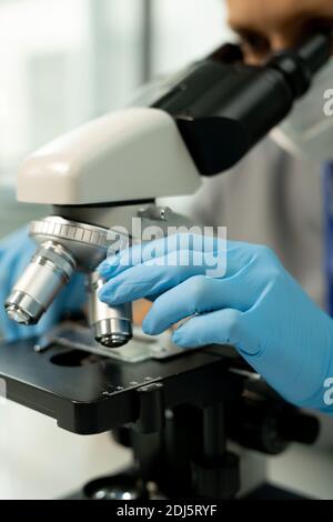 Main gantée d'un travailleur de laboratoire scientifique ou d'un chercheur qui fixe des métaux lentille de microscope pendant l'étude des échantillons chimiques Banque D'Images