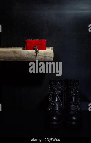 La vie d'une boîte d'argent rouge sur un bois etagère sur fond gris foncé et bottes de motard noires au sol Banque D'Images