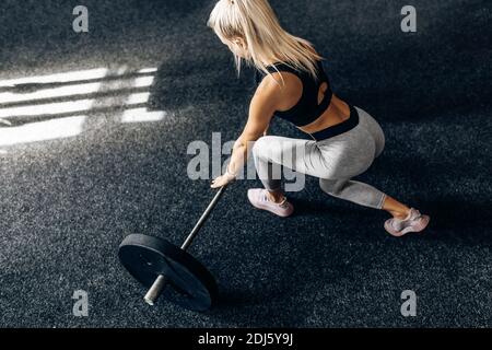 Forte femme de fitness, dans les vêtements de sport, s'entraîne avec des poids lourds dans la salle de gym, Sportswoman lève la barbell dans la salle de gym. Banque D'Images