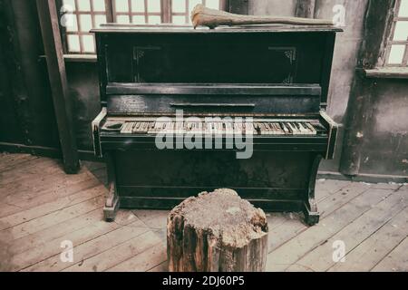 Piano cassé dans un vieux bâtiment sale. Salle en bois poussiéreuse avec un instrument de musique oublié Banque D'Images