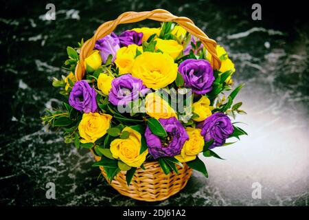 Un beau bouquet de fleurs sur le marbre noir. Roses jaunes et violettes dans un panier en osier. Composition inhabituelle de fl. Bleu et jaune collectés Banque D'Images