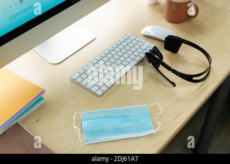 Lieu de travail d'un représentant de l'assistance clientèle moderne avec écran d'ordinateur, clavier, souris, casque, masque et mug avec boisson Banque D'Images