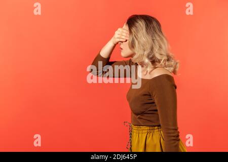 Le portrait de la jeune jolie femme en blouse brune ne voulait rien voir et couvrait ses yeux avec la main. Concept stressé ou effrayé. Banque D'Images