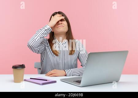 Contrarié frustrée femme employée de bureau dans une chemise rayée touchant le visage avec la main faisant geste de visage assis à l'ordinateur portable, difficultés au travail, erreur Banque D'Images