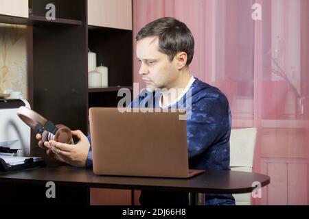 Un homme dans les vêtements de la maison travaille à un ordinateur portable. Met un casque sur la tête. Banque D'Images