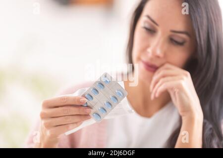 La femme envisage de prendre une pilule en regardant le blister. Banque D'Images