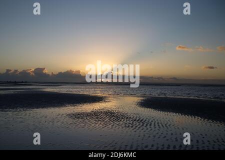Un beau coucher de soleil et des reflets dans l'eau de l'Ouest Plage de Wittering avec les rayons de soleil débordant sur le nuage sur l'horizon derrière le contour Banque D'Images