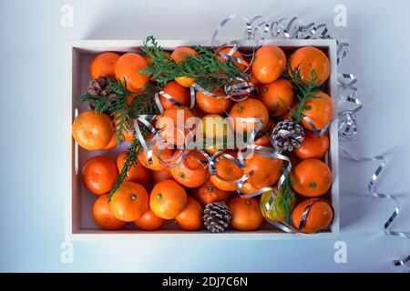 Boîte de mandarines décorée de branches de cyprès et de tingel sur une table blanche, vue du dessus. Concept Noël et nouvel an Banque D'Images