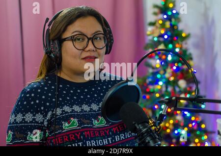 Une dame portant un pull de Noël et portant un casque chantant dans un microphone, enregistrant des voix pour une chanson. Banque D'Images