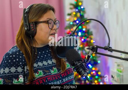 Une dame portant un pull de Noël et portant un casque chantant dans un microphone, enregistrant des voix pour une chanson. Banque D'Images