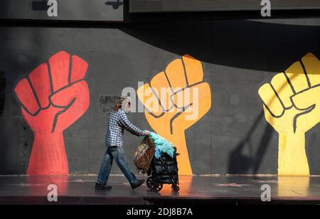 Homme sans-abri poussant un chariot devant une murale représentant des poings élevés colorés sur Hollywood Blvd. À Los Angeles, CA Banque D'Images