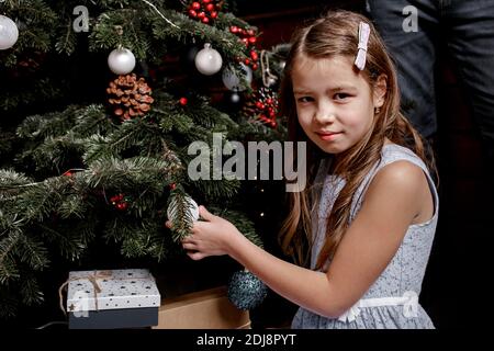 La petite fille décorera l'arbre de Noël dans le salon à la maison. Un enfant mignon se prépare à la maison pour fêter Noël. Vacances d'hiver et concept de personnes Banque D'Images