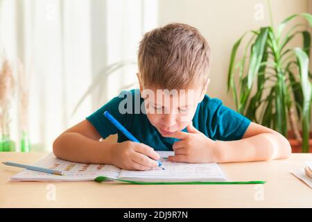 un écolier de 7 ans fait des cours de mathématiques assis à son bureau. Concept de homeschooling, apprentissage à distance Banque D'Images