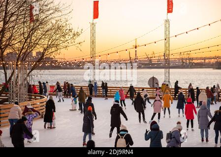 Saint-Pétersbourg, Russie - 9 décembre 2020 : un groupe de personnes patinent sur la patinoire contre le ciel du coucher du soleil au port de Sevkabel. Banque D'Images