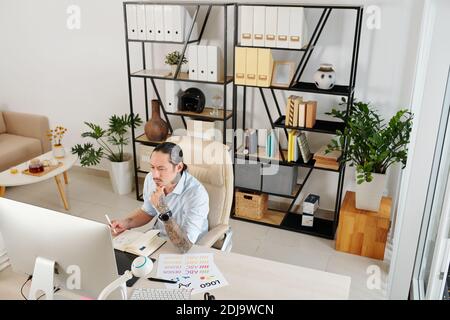 Sérieusement frognant graphiste indépendant travaillant sur l'ordinateur à table dans son bureau à domicile Banque D'Images