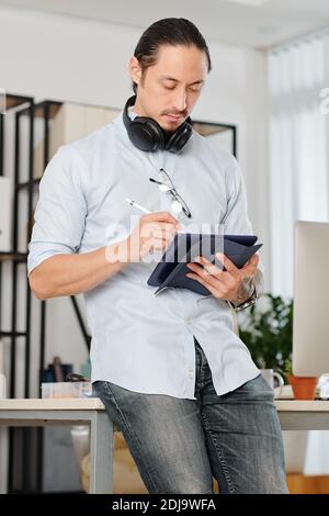 Un graphiste professionnel pensif avec un casque autour de son cou incliné bureau et tablette numérique Banque D'Images