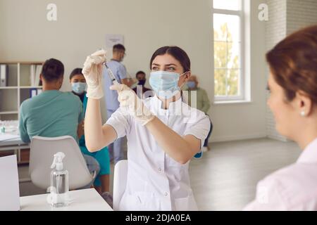 Jeune infirmière dans le masque facial tirant le vaccin hors du flacon avant de donner le tir au patient Banque D'Images