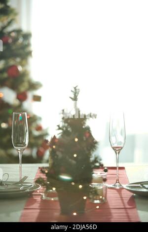 Gros plan de la table de Noël avec chemin de table rouge, flûtes à champagne et assiettes servies dans le salon Banque D'Images
