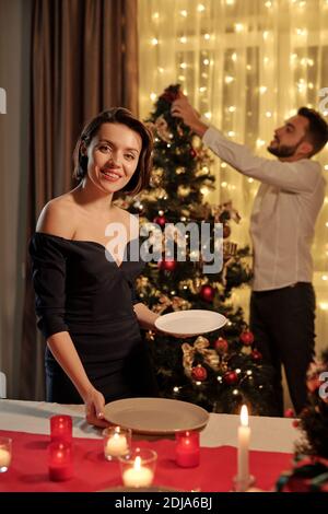 Portrait d'une fille attrayante heureuse dans une assiette à vêtements tendance Sur la table tout en préparant le dîner de Noël avec un petit ami Banque D'Images