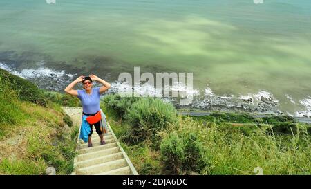 Une femme (61) fait une pause sur une section abrupte de la piste d'escarpement de Paekakariki, Île du Nord en Nouvelle-Zélande Banque D'Images