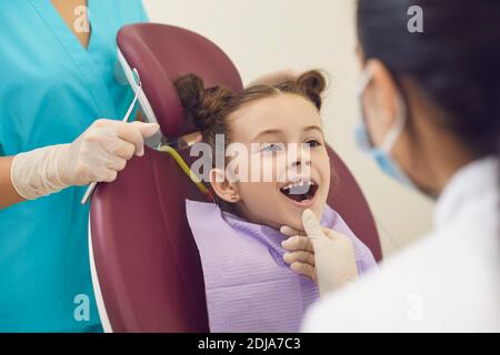 Femme dentiste examinant les dents souriantes des filles dans la bouche ouverte dedans clinique dentaire Banque D'Images