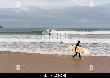Baleal, Beira Litoral - Portugal - 13 décembre 2020 : surfeur marchant sur la plage de Baleal et regardant d'autres surfeurs attraper des vagues Banque D'Images