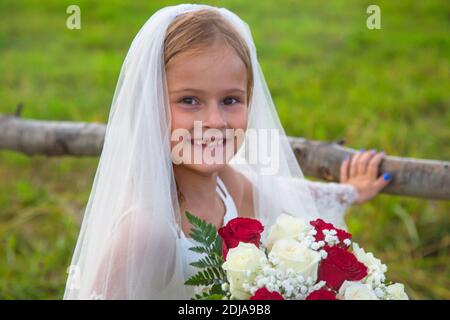 ove est présent. Jour des enfants. Petite fille en robe de mariée avec un voile et un bouquet de mariage. Beauté. Une petite fille avec un bouquet de rouge et blanc Banque D'Images