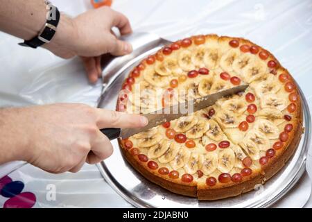 L'homme coupe une tarte maison couchée sur une planche ronde en morceaux avec un couteau. Banque D'Images