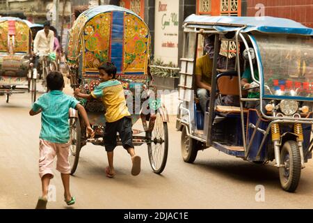 Dhaka, Bangladesh - 28 octobre 2018 : deux enfants jouant et essayant de monter à bord d'un pousse-pousse, le moyen de transport urbain le plus courant. Banque D'Images