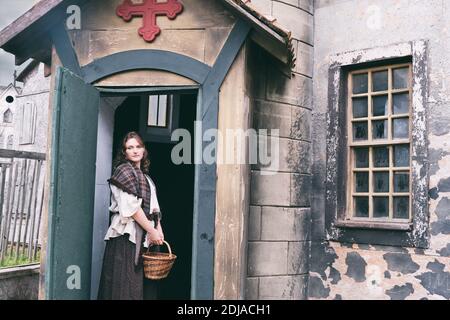 Femme en robe rétro dans la cour d'une vieille église avec une croix au-dessus de la porte, vêtements sur Halloween Banque D'Images