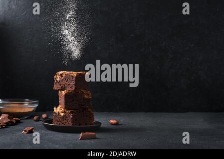 Pile de brownies sur fond noir. Délicieux dessert au chocolat maison, brownie avec sucre en poudre, espace de copie. Banque D'Images