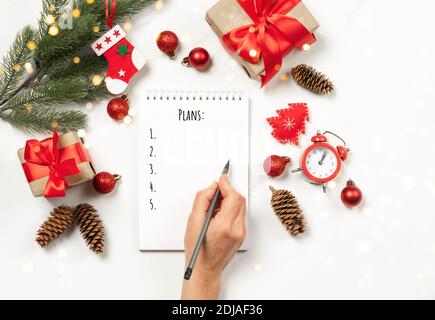 La main féminine écrit les plans d'objectifs dans un cahier vierge. Jouets boîte cadeau de Noël sur fond blanc. Concept du nouvel an festif. Co Banque D'Images